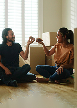 Couple sitting on floor surrounded by boxes and eating pizza