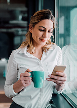 A women looking at her phone and holding a cup 