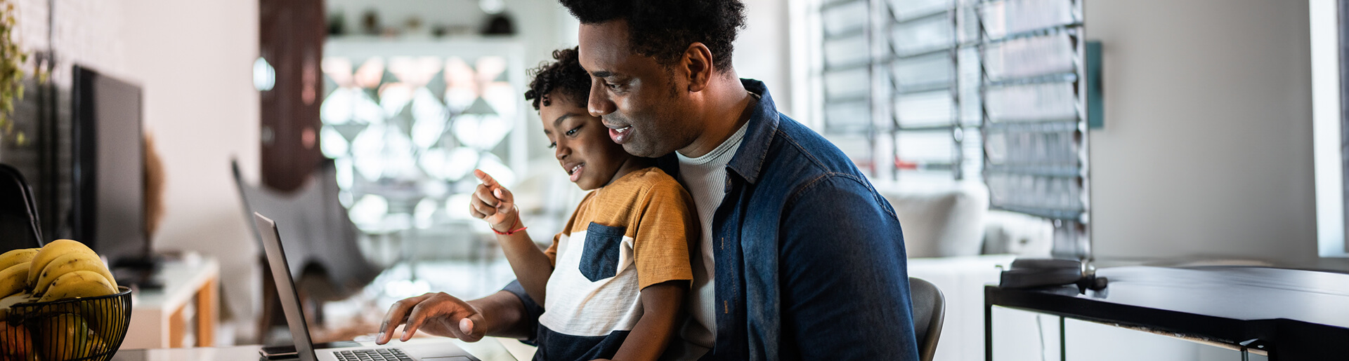 Dad looking at laptop screen with son on his lap