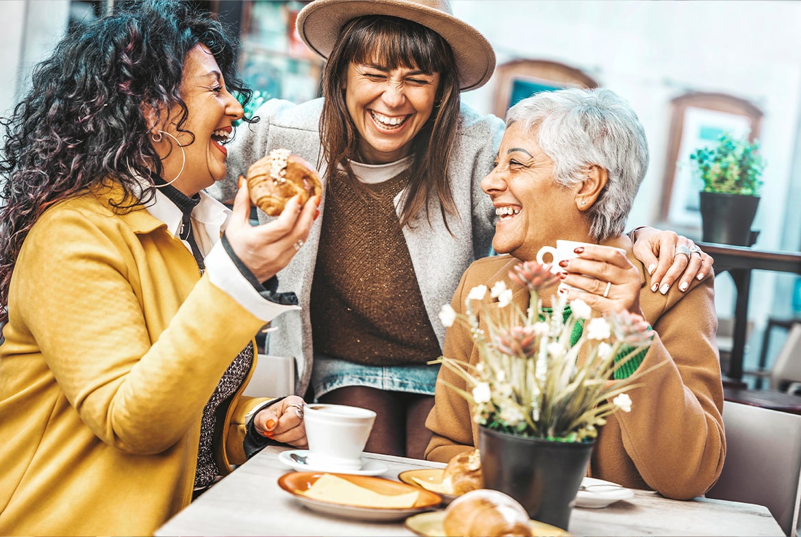 Three middle aged women laughing at a cafe together