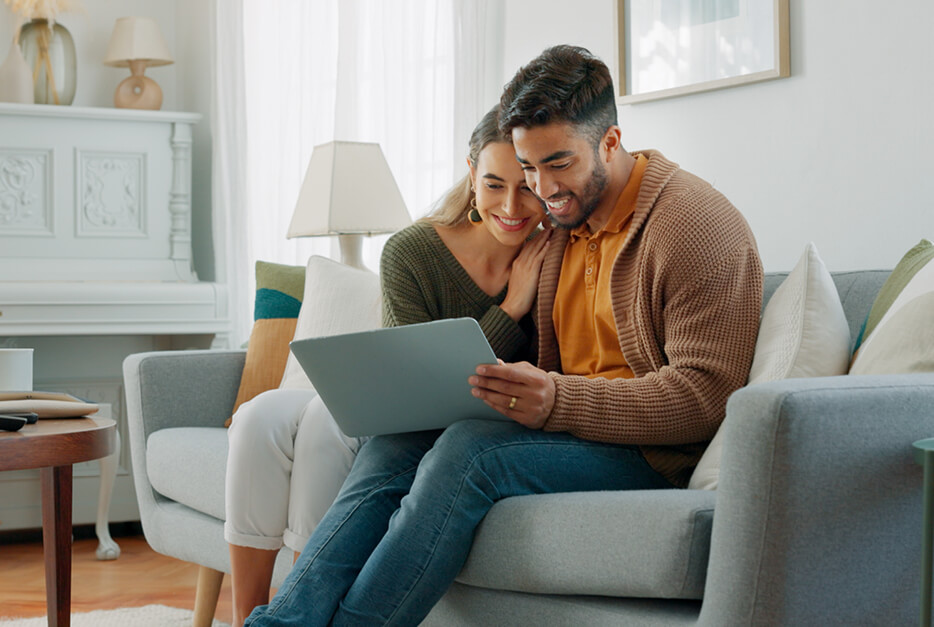 Couple sitting on a couch looking at a laptop