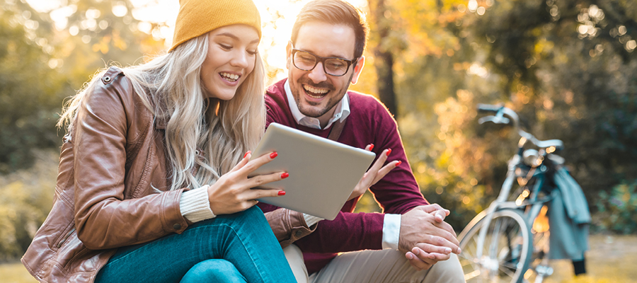 Two people sitting on a concrete bench, looking at tablet together