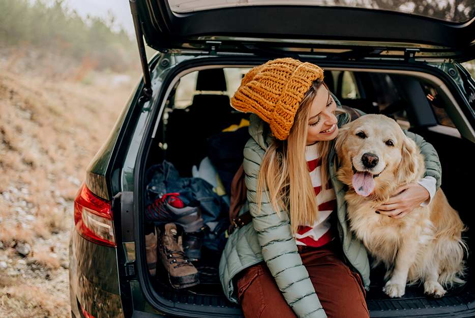 Young woman sitting in the back of her car with her dog