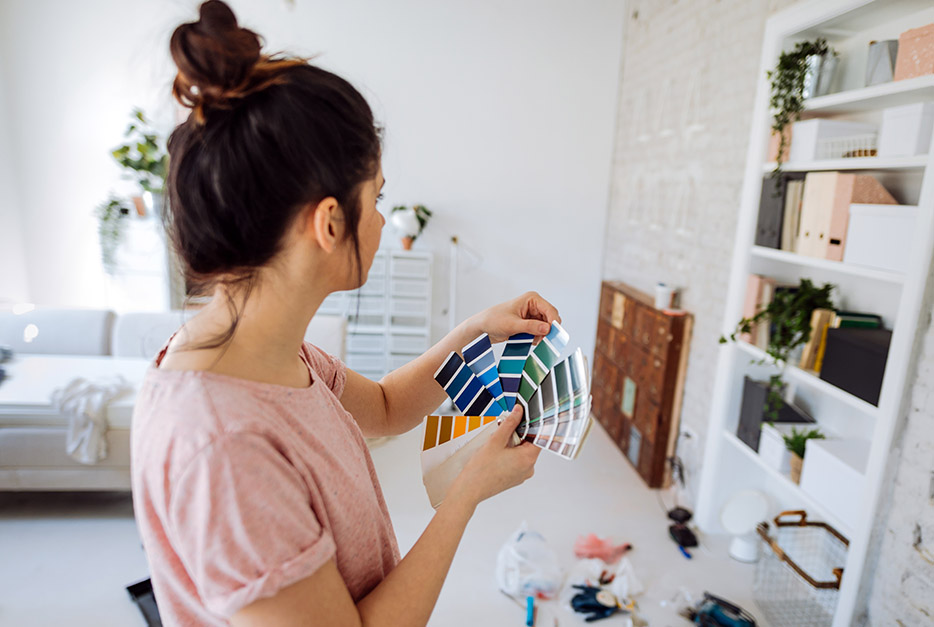 Woman holding a paint swatch in front of her wall