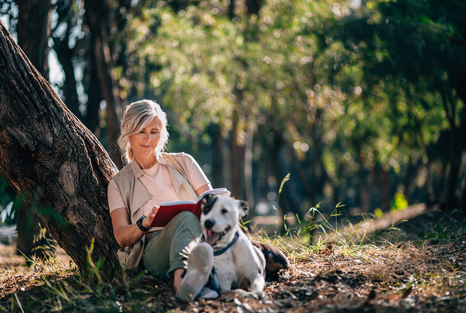 Woman sitting with her dog outside reading a book