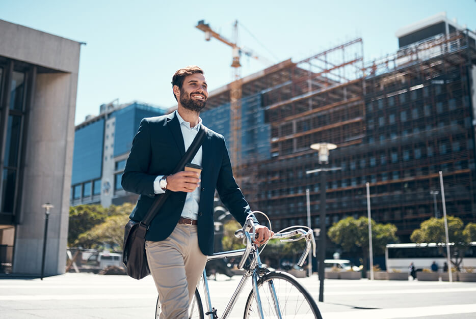 Young guy in suit walking his bicycle and drinking a coffee