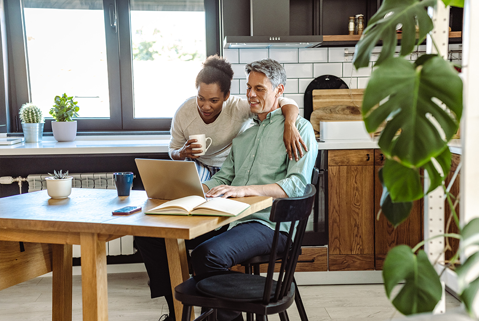 Man and woman sitting at kitchen table looking at a computer