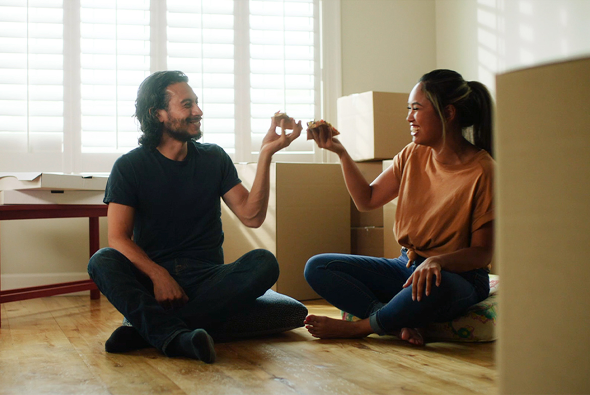 young couple eating pizza with moving boxes